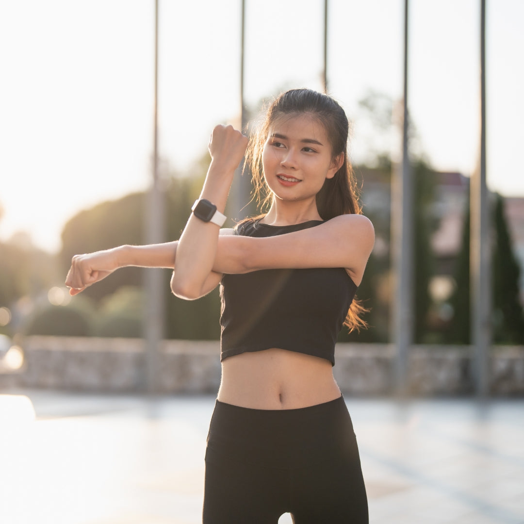 Woman in black athletic wear stretching outdoors with a blurred background