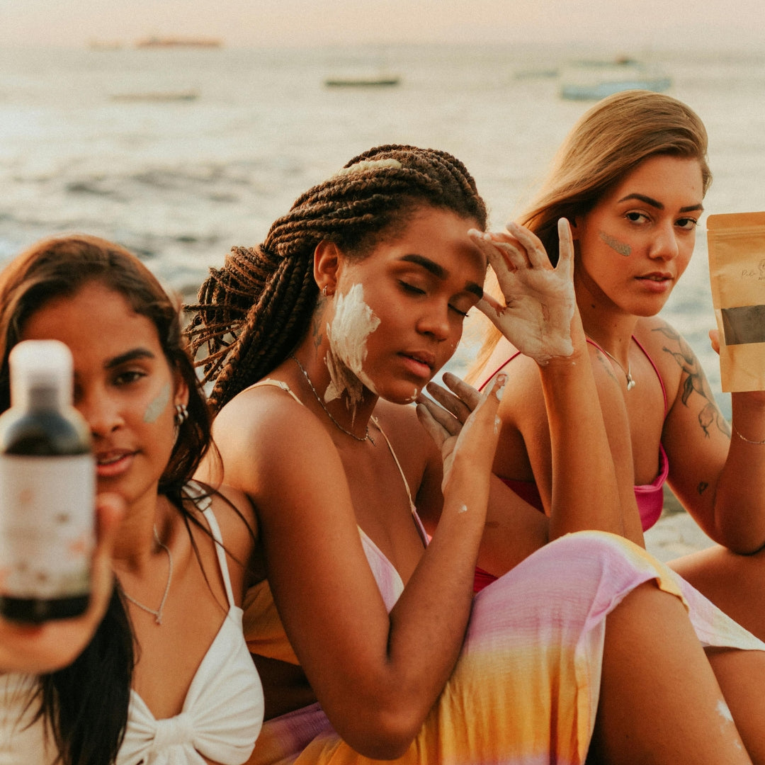 Three women applying sunscreen on a beach with a bottle of sunscreen in the foreground.